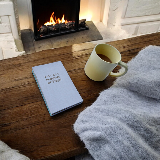 pocket promises of prayer devotional on a wood table with a yellow coffee mug by a fireplace